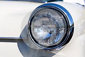 Close-up of the round headlamps of a white classic car.