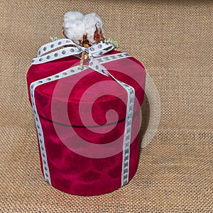 Close-up round red gift box with white bow and cotton flowers on a sackcloth background. Holiday concept