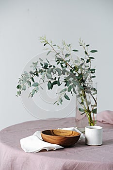 Close up of a round table with a rough pale pink tablecloth and branch in a jar