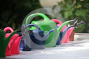 a Close-up of a row of colorful watering cans of various sizes on a table in the greenhouse