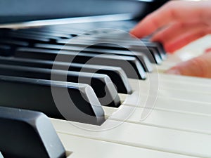 A close-up of a row of piano keys. In the blurred background, a pianist's hands can be seen practicing on the piano.