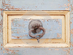 Close up of Rusted iron ring handle on peeling and eaten old wooden door. Construction and architectural details