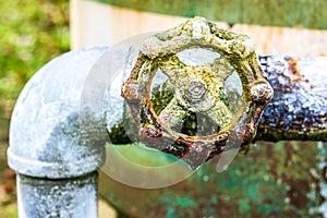 A close up of a rusted valve connects to water supply with metal pipe,Industrial metal water tab,seen in a garden