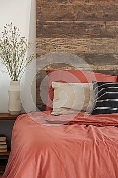 Close-up of a rustic bed with wooden bedhead and red bedding in bright bedroom interior. Real photo