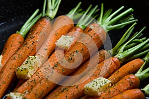 Close up of rustic carrotts in a pan with butter on wood