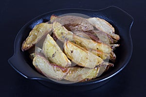 Close up rustic roasted potatoes on black plate on black background