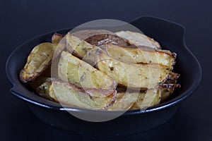 Close up rustic roasted potatoes on black plate on black background