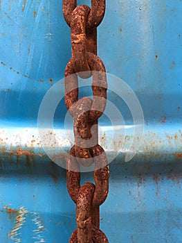 Close-up of a rusty chain in front of blue rusty steel drum