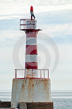 Close up of a rusty old red and white striped harbor lighthouse at the end of a jetty