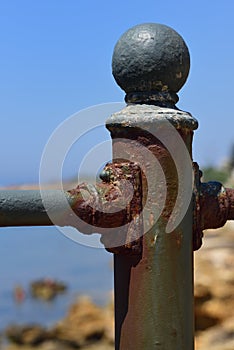 Close up of a rusty and weathered metal post, against a blue sky and sea, in portrait format