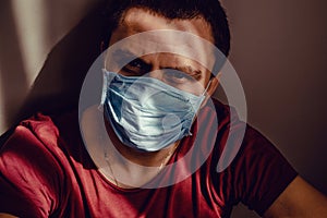 Close up sad thoughtful adult man portrait in medical mask sit leaning on wall with stare eyes. Stay isolation at home. Quarantine