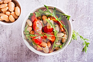 Close up of salad of canned white beans, cherry tomatoes and arugula in a bowl top view