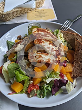 Close-up of a salad with pumpkin, lettuce, tomatoes, pomegranate and halloumi cheese with slices of bread