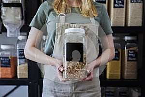Close Up Of Sales Assistant In Sustainable Plastic Free Wholefood Store Holding Container With Blank Label