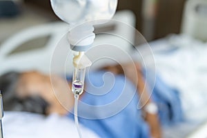 A close-up of a saline bottle strapped to a needle pricked at the hand of a female patient lying in a hospital bed. Medical and tr