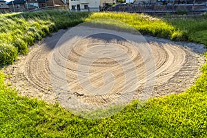 Close up of a sand trap surrounded by grasses at a golf course on a sunny day