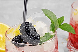 Closeup of a glass of fruit juice, succulent blackberries, green sappy leaves of mint on a light blurred background.