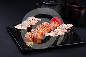 Close up of sashimi sushi set with chopsticks and soy on black background. Korea rolls and green tea cups and teapot, copy space.