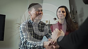 Close-up of satisfied Caucasian client shaking psychologist`s hand. His happy beautiful wife or girlfriend sitting next