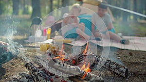 Close up of sausages and corn on skewers being cooked on fire with smoke during summer family camping vacation with tent