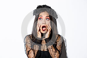 Close-up of scared asian woman in halloween costume of witch looking frightened at upper left corner, gasping and