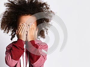 Close up of scared little african child shyly or terrified covering face with hands.
