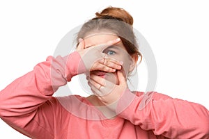 Close up scared teen girl hiding face in palms hands and peering out with one eye between her fingers, trembling fear