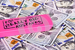 Close up scattered US Dollars with message on pink eraser for really big mistake. Fixing financial, business, taxes problems