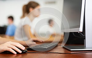 Close-up schoolgirl using computer mouse with computer keyboard in computer class