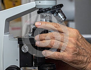 Close-up of scientist adjusting microscope in laboratory setting