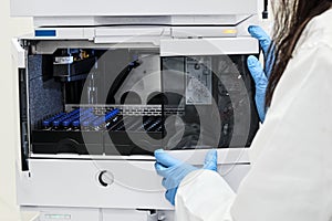 Close up scientist put sample in a glass vial with blue cap into the auto sampler rack in HPLC system. High performance liquid