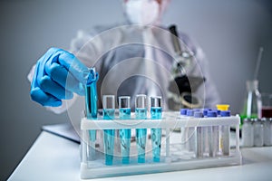 Close-up of scientists hand in blue latex gloves examines samples chemical liquid in test tube in science laboratory