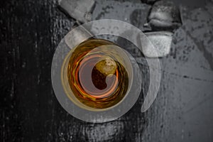 Close up of Scotch whiskey or Grain scotch in a transparent glass with ice cubes on black colored wooden surface.