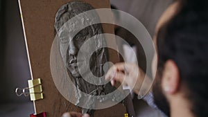 Close-up of Sculptor creating sculpture of human`s face on canvas in art studio