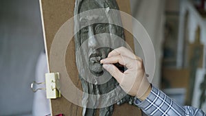 Close-up of Sculptor creating sculpture of human`s face on canvas while young woman posing to him in art studio