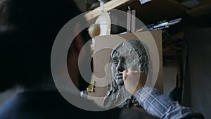 Close-up of Sculptor creating sculpture of woman`s face on canvas in art studio