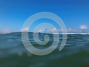 Close up of sea wave. Front view on beautiful sea wave on sandy beach. Summer sunny day, blue sky, water background. Blur effect