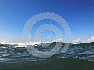 Close up of sea wave. Front view on beautiful sea wave on sandy beach. Summer sunny day, blue sky, water background