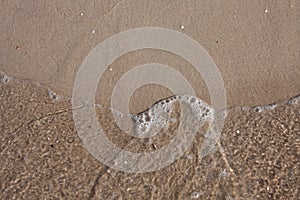 Close-up of a sea wave on a sandy beach. Top view. Sand beach texture