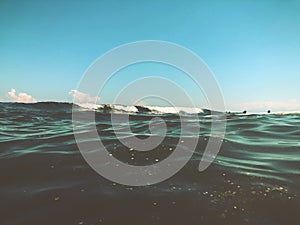 Close up of sea wave with splashes. Front view on beautiful sea wave on sandy beach. Summer sunny day, blue sky, water background