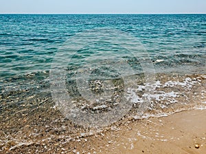 Close up sea waves stones shells beach summer day. top view above transparent water.
