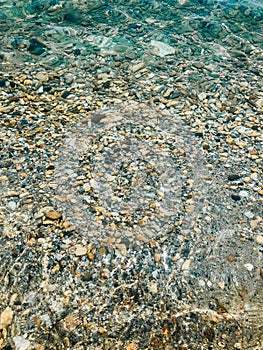 Close up sea waves stones shells beach summer day. top view above transparent water.