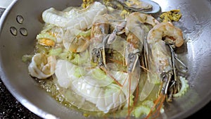 Close-up of seafood fried in a frying pan in hot oil. A professional chef cooks in the flambe style.Cooking a dish. A