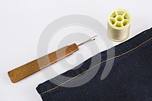 Close-up of seam ripper, spool of thread and stitched denim