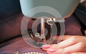 Close-up of seamstresses`s hands sews to blue jacket leather inserts on sewing mashine. Side view.