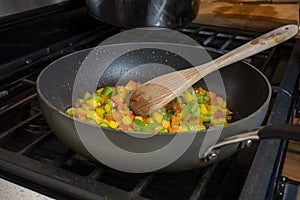 Close up, selective focus on diced bell peppers cooking in a large skillet on a gas stove top