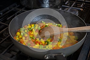 Close up, selective focus on diced bell peppers cooking in a large skillet on a gas stove top