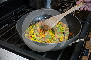 Close up, selective focus on diced bell peppers cooking in a large skillet on a gas stove top