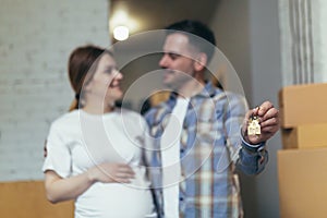 Close-up selective focus photo, man and pregnant woman together in new apartment smiling and happy holding house keys