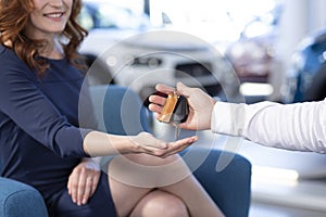 Close-up of seller giving keys of car to smiling woman after transaction in the salon